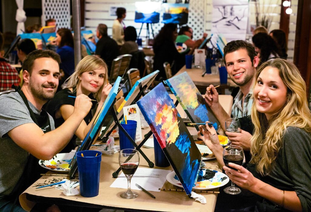 Friends enjoy a painting session at a creative workshop, each poised with brushes and colorful canvases, showcasing vibrant artwork and camaraderie.
